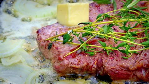 A rare piece of steak is being cooked with thyme, onions and butter. Stock Footage 317931472