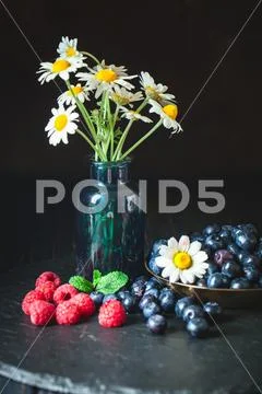 Raspberries and blueberries with chamomile and leaves on a dark background. S Stock Photos