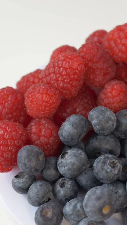 Raspberries and blueberries rotating on light background represent superfood Stock Footage 333114792