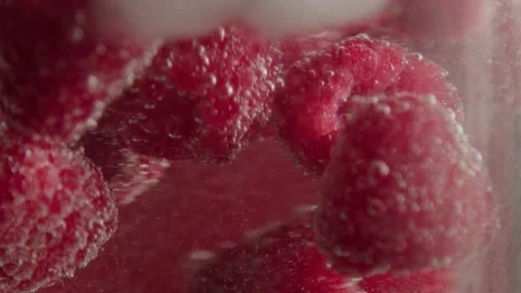 Raspberries float with ice in sparkling water in a glass on a red background. Stock Footage 170431565