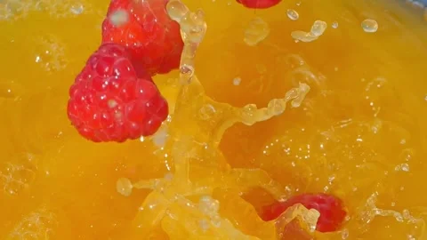 Raspberries splashing into bright orange juice, creating dynamic bubbles Stock Footage 288114537
