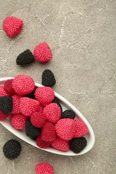 Raspberry and blackberry candy on plate on grey background. Vertical photo Stock Photos