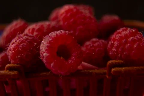 Raspberry berries lie in a plastic brown basket. filmed in a dark way. Stock Photos