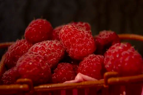 Raspberry berries lie in a plastic brown basket. filmed in a dark way. Stock Photos