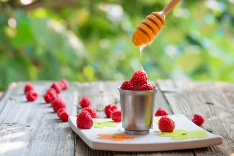 Raspberry in a cup with flowing honey from a dipper, on wood table Stock Photos