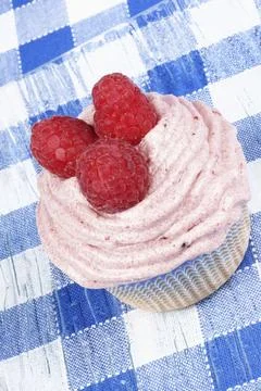 Raspberry cupcake on a glass dish over a chequered background Foto stock