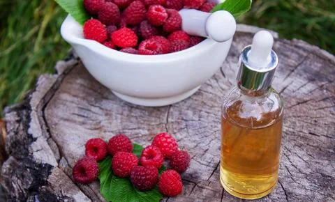 Raspberry essential oil in a bottle with fresh berries on a wooden stump. Foto stock