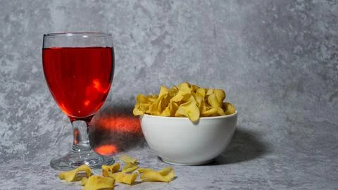 Raspberry flavored red syrup in a glass cup and cassava chips in a white pl.. Stock Photos