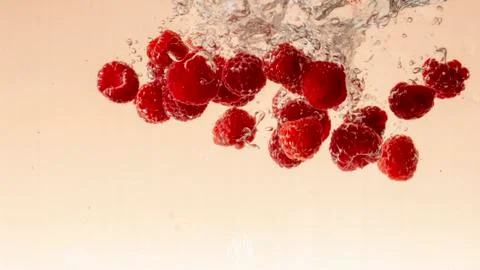 Raspberry fruits making splash in water orange pastel background Stock Photos
