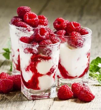 Raspberry ice cream with berries and mint, served in glasses on an old wood.. Stock Photos
