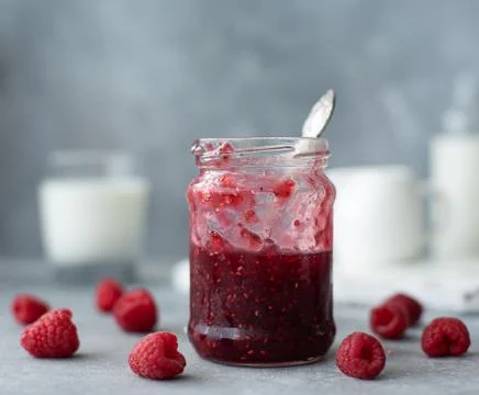 Raspberry jam in a glass jar with a spoon Stock Photos