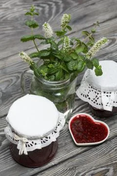 Raspberry jam in jars and a saucer. On pine planks painted black and white. N Foto stock
