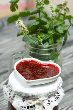 Raspberry jam in jars and a saucer. On pine planks painted black and white. N Foto stock