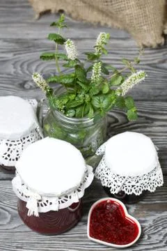 Raspberry jam in jars and a saucer. On pine planks painted black and white. N Foto stock