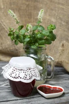 Raspberry jam in jars and a saucer. On pine planks painted black and white. N Foto stock