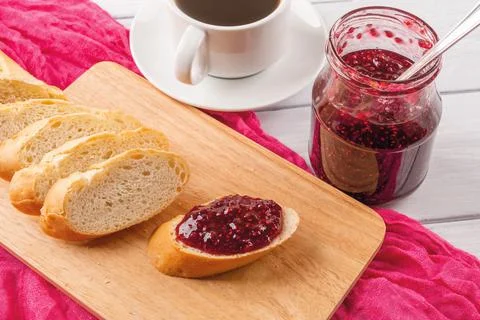 Raspberry jam sandwich on a cutting board, jam jar and cup of tea or coffee. Stock Photos