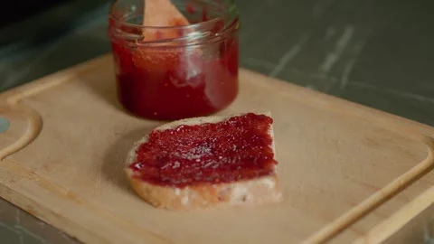 Raspberry jam spread on a slice of bread in a home kitchen setting 스톡 동영상 320952003