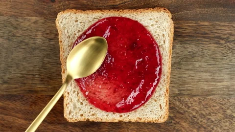 Raspberry jam spreading on bread with a golden spoon Video stock 233971295