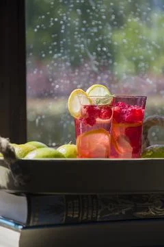Raspberry lime lemonade on the windowsill, outside the window rain and sun Stock Photos