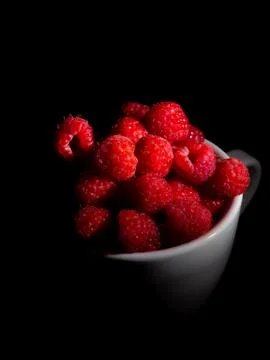 Raspberry in a mug on a black background. Stock Photos