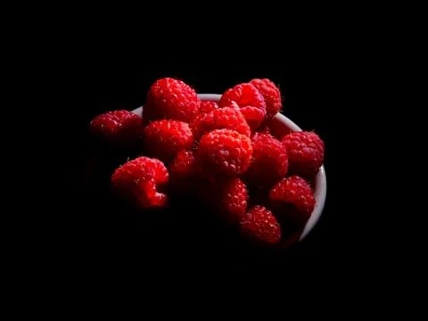 Raspberry in a mug on a black background. Stock Photos