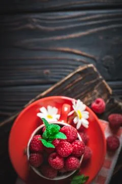 Raspberry in a red cup with chamomile and leaves on a dark background. Summer Foto stock