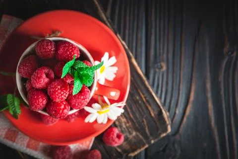 Raspberry in a red cup with chamomile and leaves on a dark background. Summer Foto stock