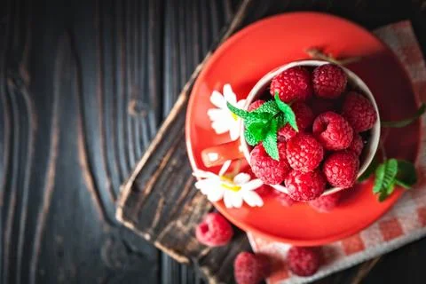 Raspberry in a red cup with chamomile and leaves on a dark background. Summer Foto stock