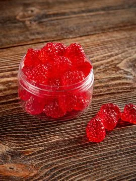 Raspberry-shaped sweets in a clear glass jar. Brown wooden background. Stock Photos