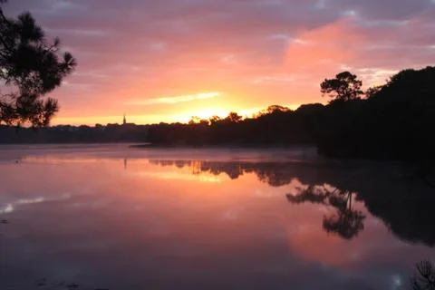 Raspberry sunset over the quiet surface of the lake Stock Photos