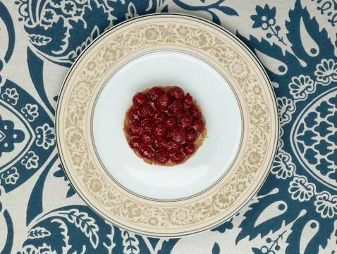 Raspberry tartlet in plate against patterned background Stock Photos