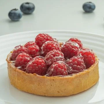 Raspberry tartlets served on a transparent plate with brown sugar. Glass of m Stock Photos