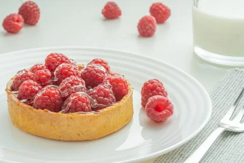 Raspberry tartlets served on a transparent plate with brown sugar. Glass of m Stock Photos