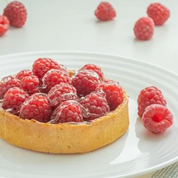 Raspberry tartlets served on a transparent plate with brown sugar. Glass of m Stock Photos