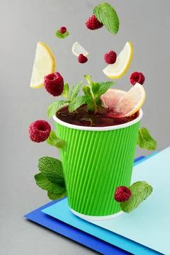 Raspberry tea in paper green cup with flying ingredients on gray background Stock Photos