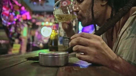 Rasta man smoke weed drinks beer at a reggae bar hippie vintage style night time Video stock 278532607