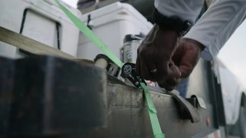 Ratcheting down coolers with green tie down strap onto truck trailer, Stock Footage 234294878