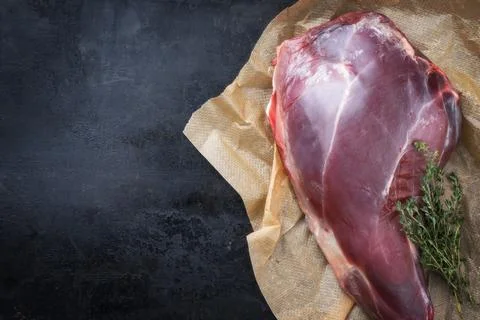 Raw aged leg of venison with bone and thyme as top view on brown paper with c 스톡 사진