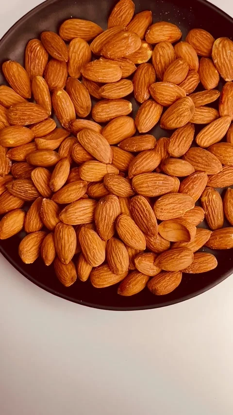 Raw almond nuts in black plate, white background, vertical format, top view Stock Footage 336471541