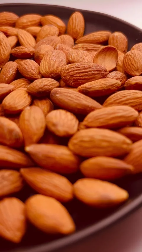 Raw almond nuts in black plate, white background, vertical format, close up view Stock Footage 336471542