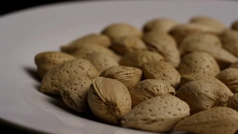 Raw almond nuts in shells on white plate surface Stock Footage 327829355