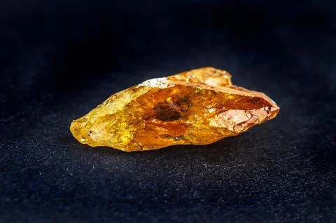Raw amber resin chunk with translucent golden-orange hues on a dark texture.. Stock Photos