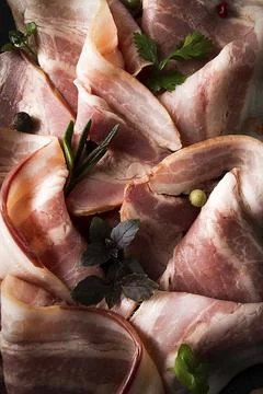 Raw bacon, sliced, with micro greenery and spices, on a black background, Foto stock