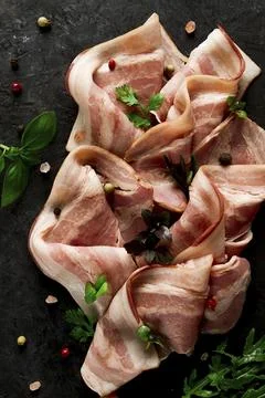 Raw bacon, sliced, with micro greenery and spices, on a black background, Foto stock