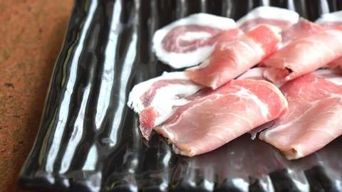 Raw bacon slices on a black grill rack 库存照片