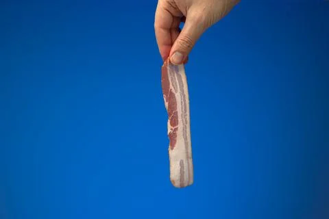 Raw bacon strip or slice held between finger by Caucasian male hand. Close up Fotos de archivo