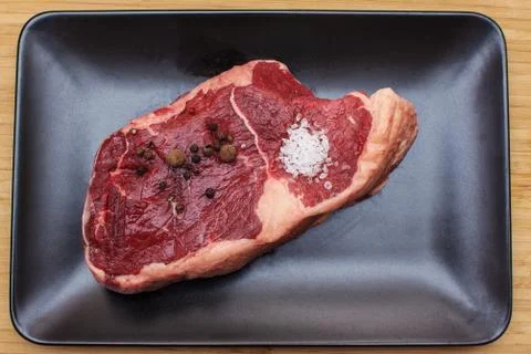 Raw beef on a black plate. Stock Photos