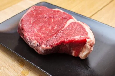 Raw beef on a black plate. Stock Photos