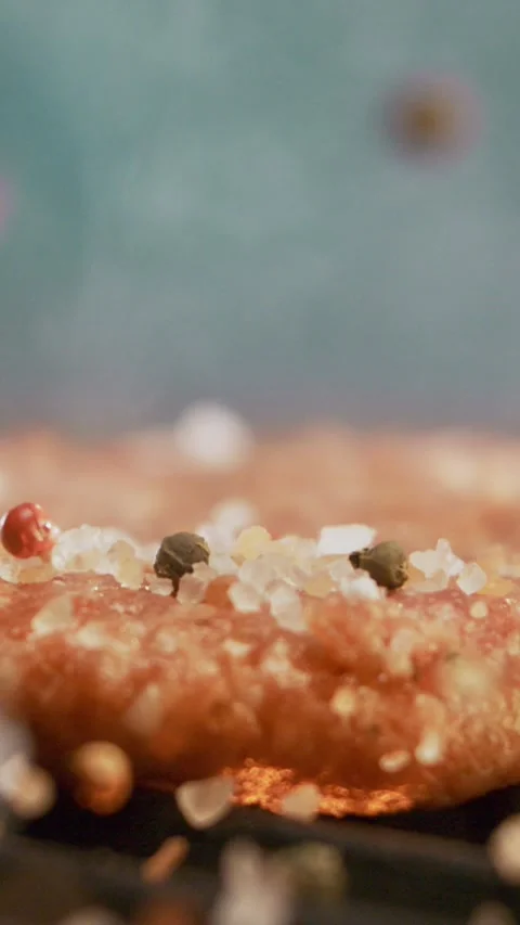 Raw beef burger patty being seasoned with colorful peppercorns and sea salt.. Stock Footage 337475544