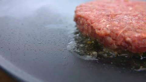 Raw beef cutlet for a burger is frying on the flat grill surface Stock Footage 133892458